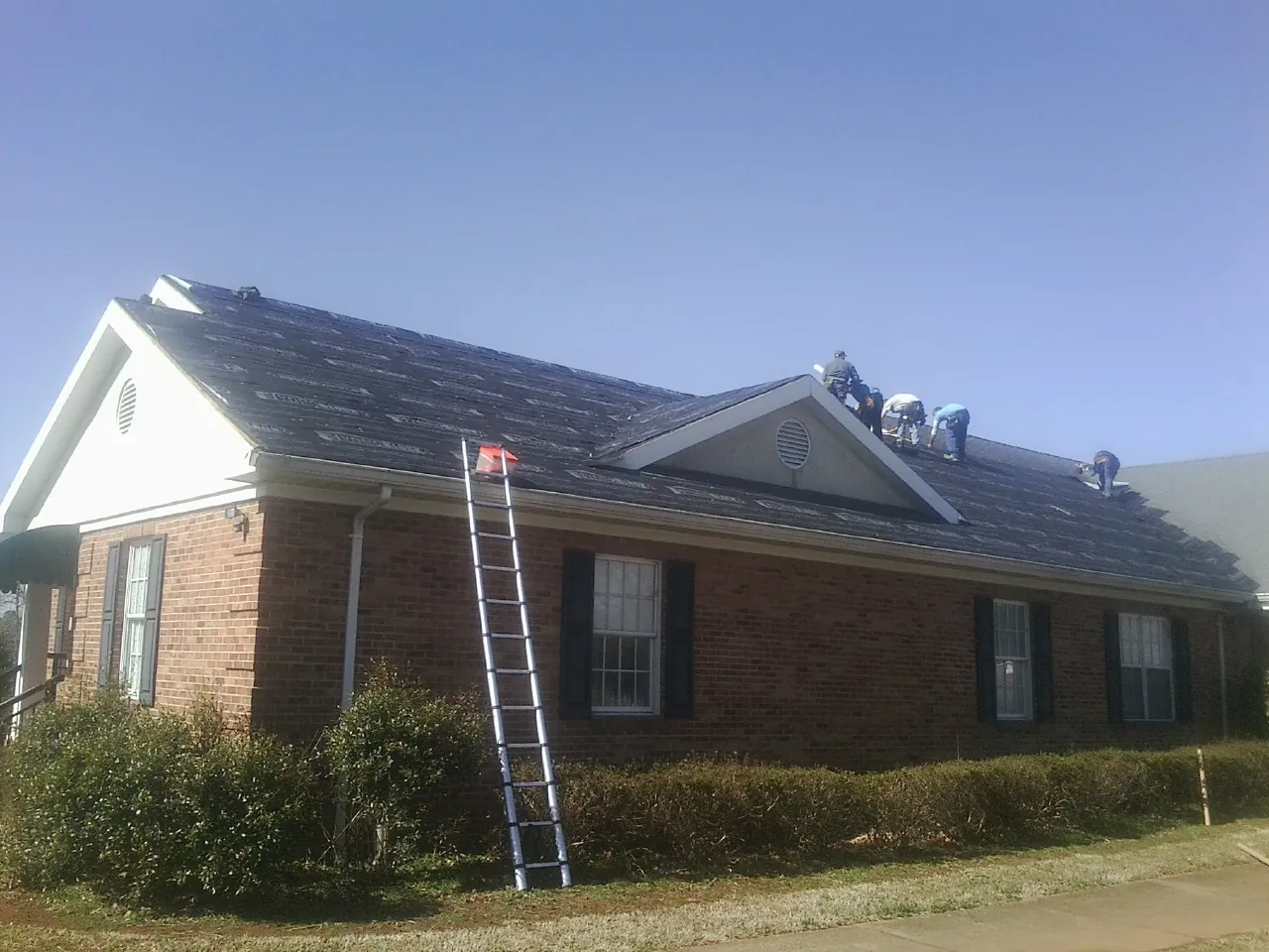 Crew tearing shingles off a brick ranch roof with a ladder set — Emergency Roof Repair work by our crew in Northboro