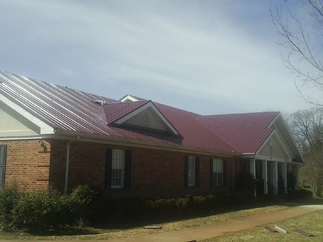 Red metal roof with gabled entries on a long brick building, from a Hail Damage Roof Repair job in Northboro