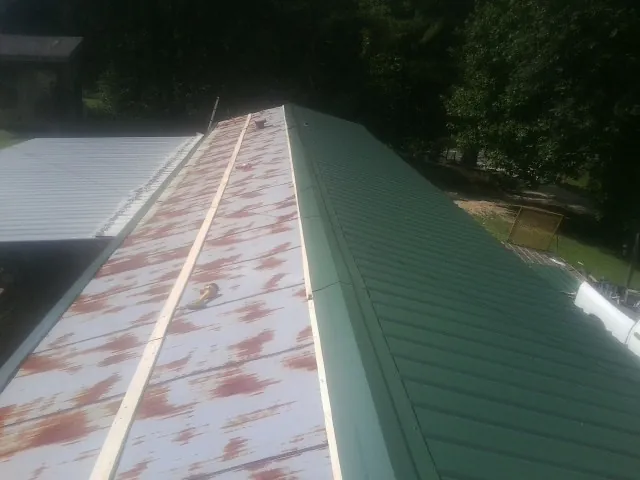 Old rusted panels beside newly installed green metal roofing — Wind Damage Roof Repair by Roofing Brothers in Northboro