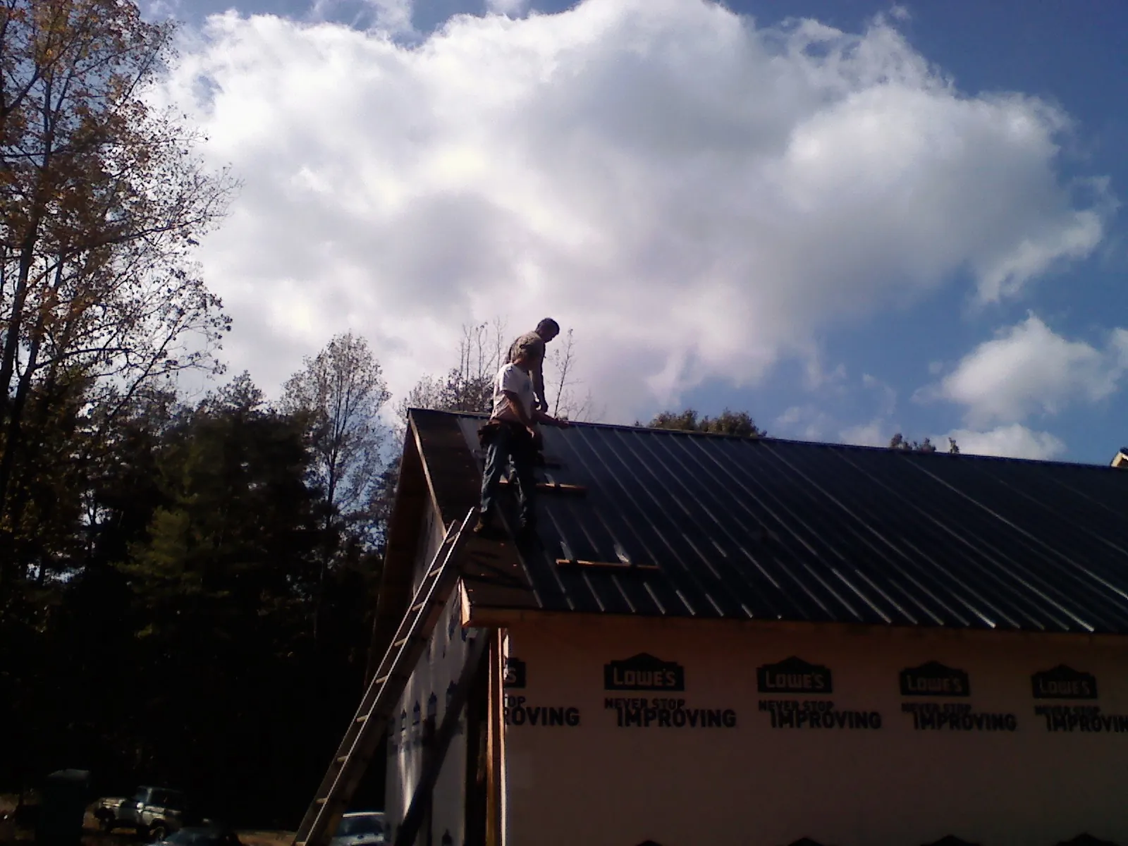 Roofer fastening dark metal panels high against a cloudy sky, from a Roof Inspection job in Northboro
