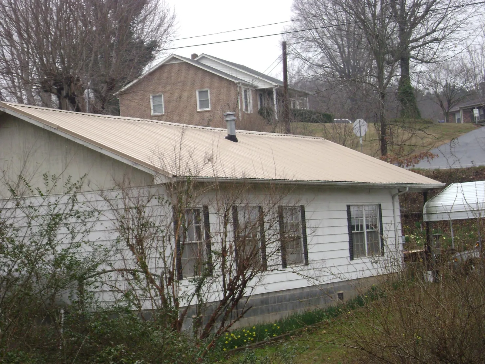 Tan metal roof on a white sided house set into a hillside — Commercial Roofing by Roofing Brothers in Northboro